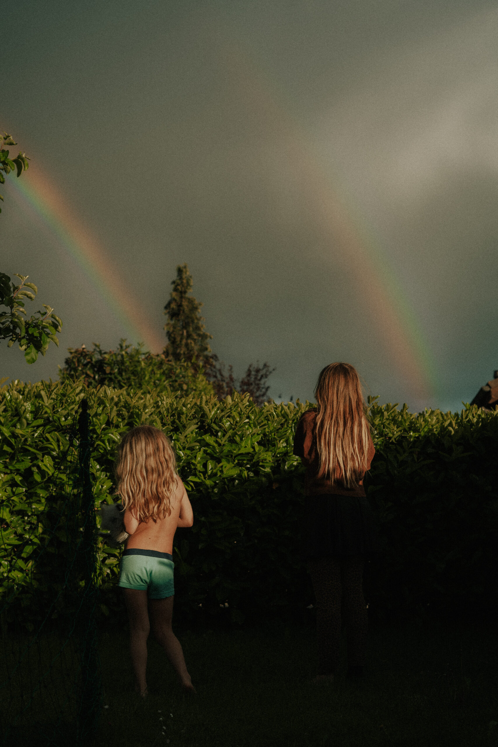 Fr&egrave;re et soeur avec leurs poules devant un arc-en-ciel
